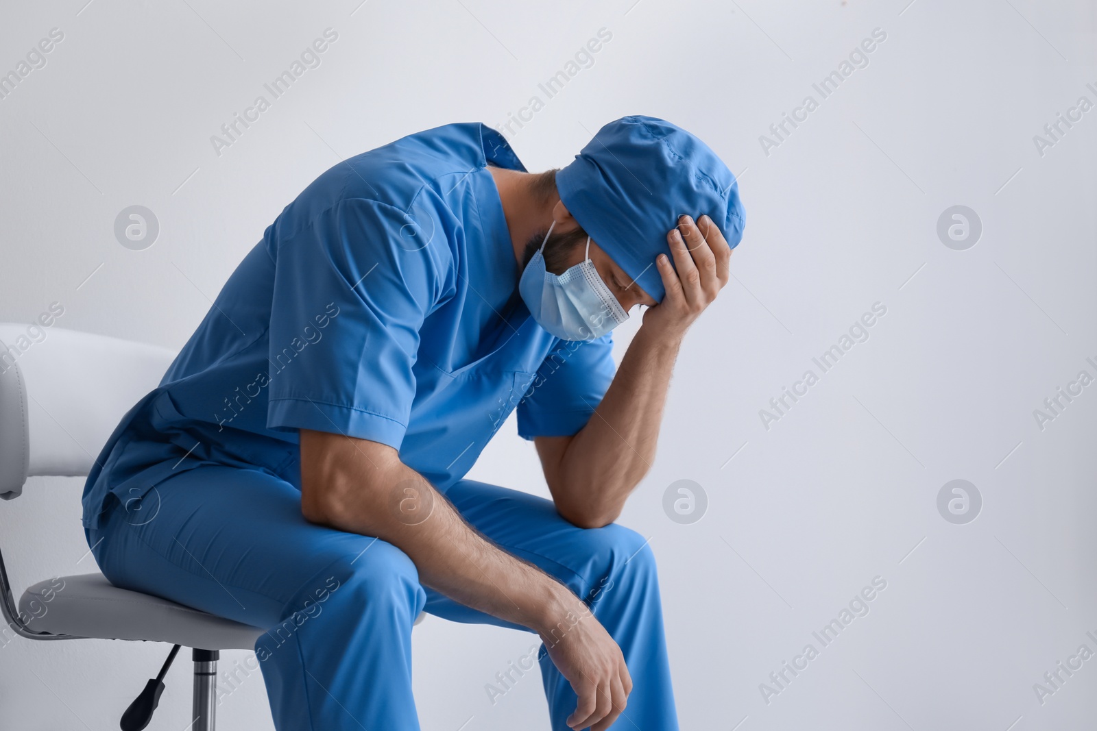 Photo of Exhausted doctor sitting on chair against light background. Stress of health care workers during COVID-19 pandemic