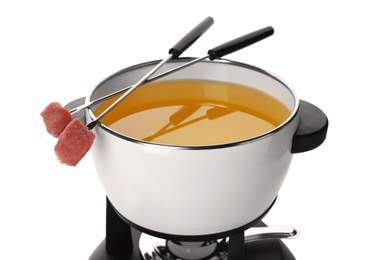 Fondue pot with oil and raw meat on forks against white background