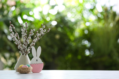 Photo of Easter bunny figure and dyed eggs on white wooden table against blurred green background. Space for text