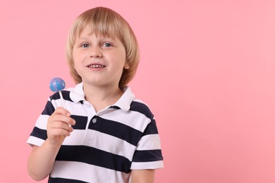 Photo of Happy little boy with lollipop on pink background, space for text