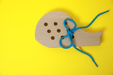 Photo of Wooden figure with holes and lace on yellow background, top view. Educational toy for motor skills development