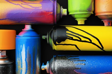 Photo of Used cans of spray paints on black background, flat lay. Graffiti supplies