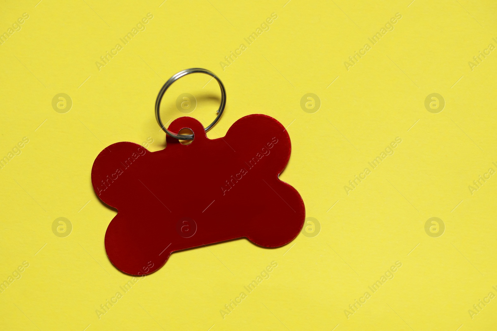 Photo of Red metal pet tag in shape of bone with ring on yellow background, top view. Space for text
