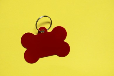 Photo of Red metal pet tag in shape of bone with ring on yellow background, top view. Space for text