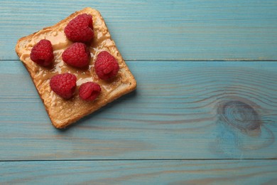 Photo of Delicious toast with peanut butter and raspberries on light blue wooden table, top view. Space for text