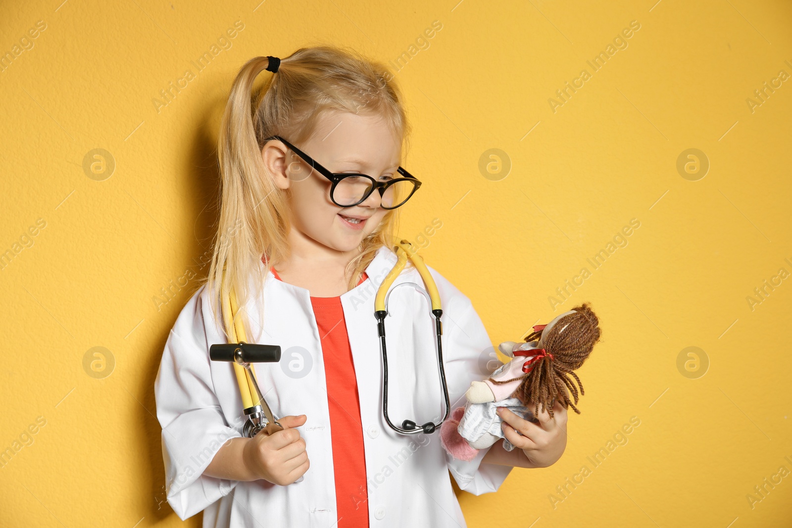 Photo of Cute child imagining herself as doctor while playing with reflex hammer and doll on color background