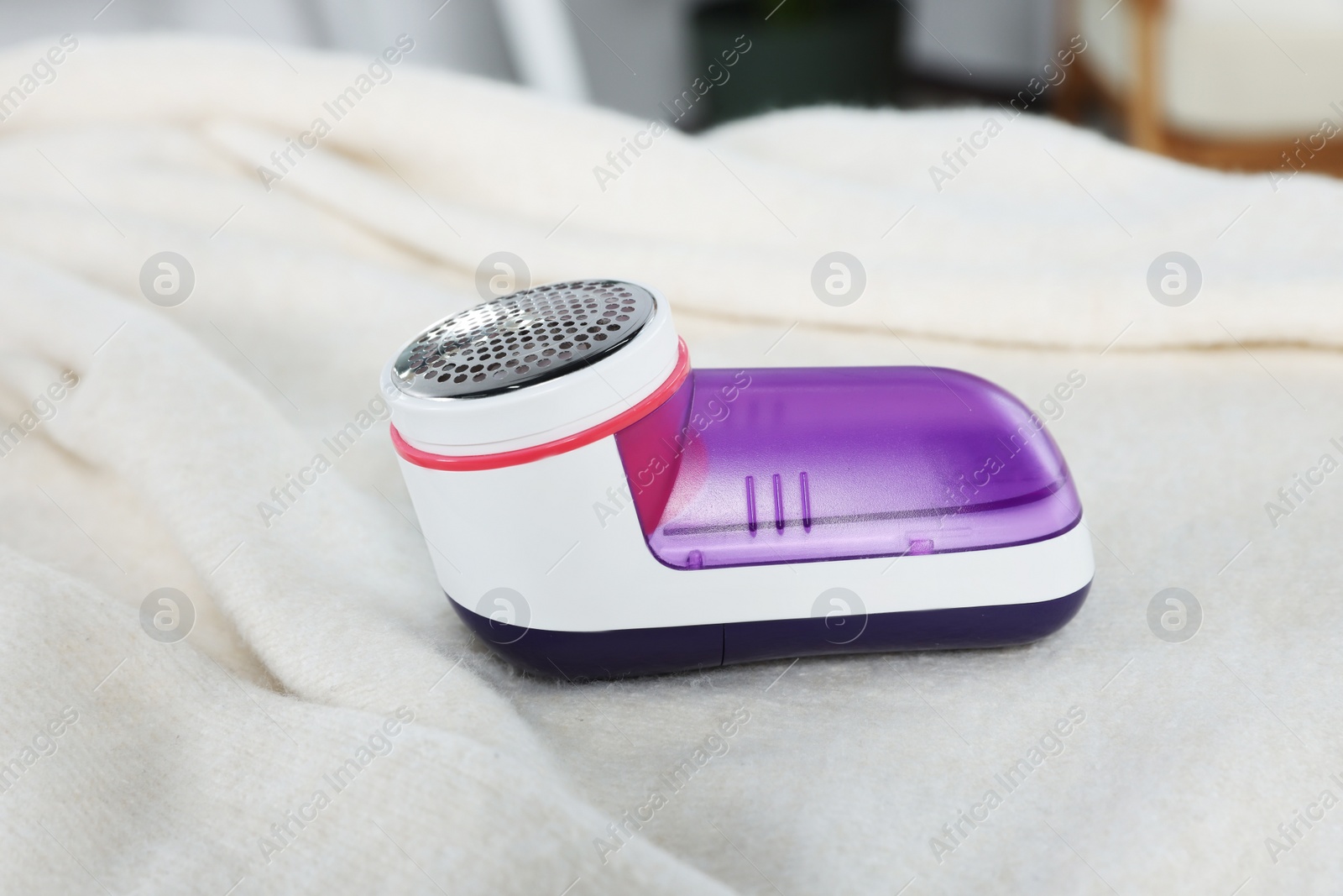 Photo of Modern fabric shaver on beige cloth indoors, closeup