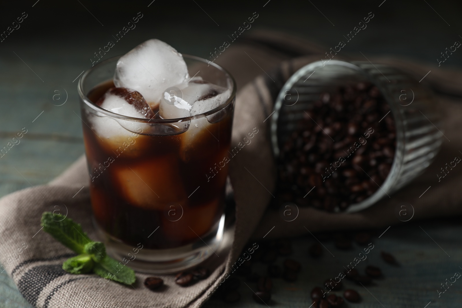 Photo of Glass of delicious iced coffee, mint and beans on table, closeup. Space for text