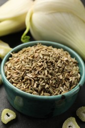 Fennel seeds in bowl, whole and cut vegetables on table, closeup