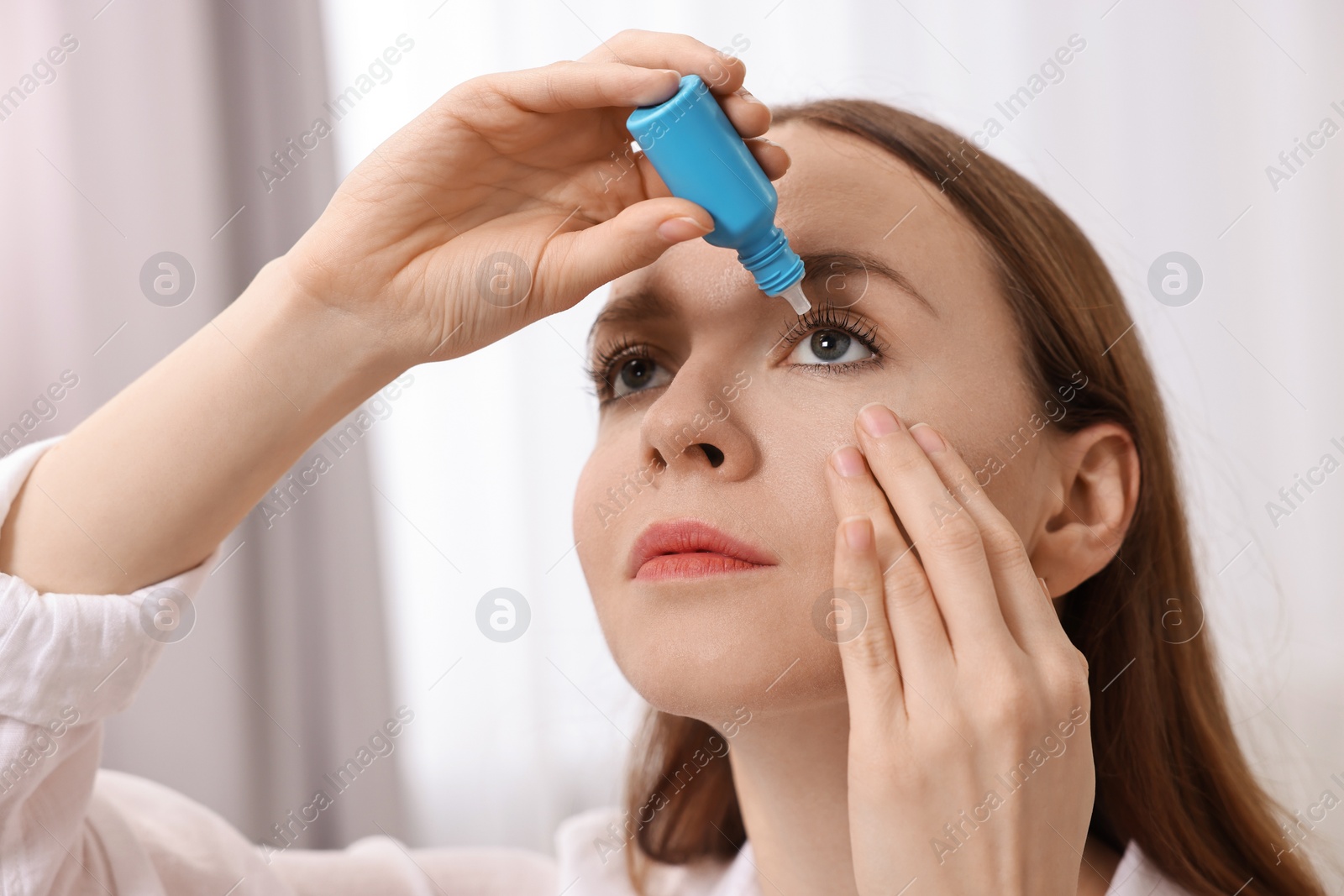 Photo of Young woman applying medical eye drops indoors