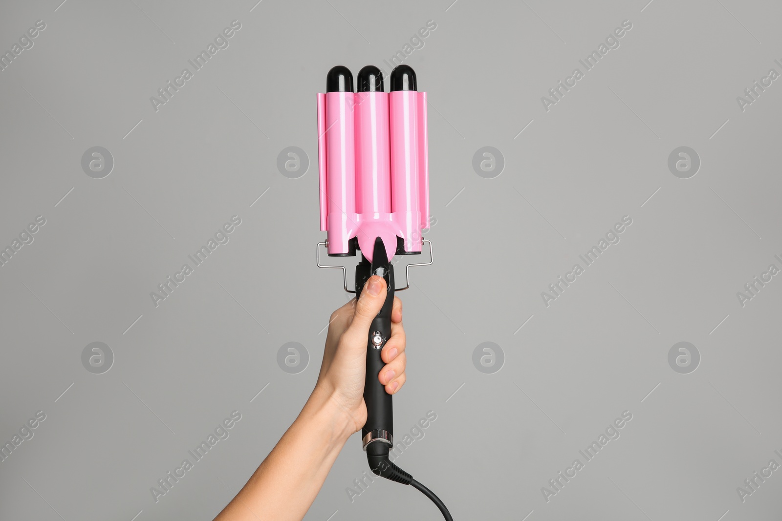 Photo of Woman holding triple curling hair iron on light grey background, closeup