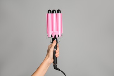 Woman holding triple curling hair iron on light grey background, closeup