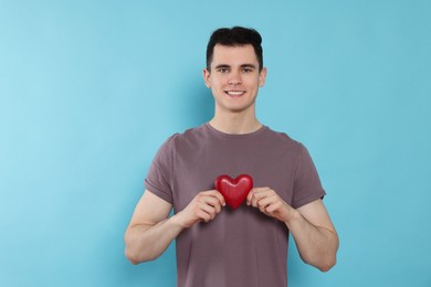 Photo of Happy volunteer holding red heart with hands on light blue background