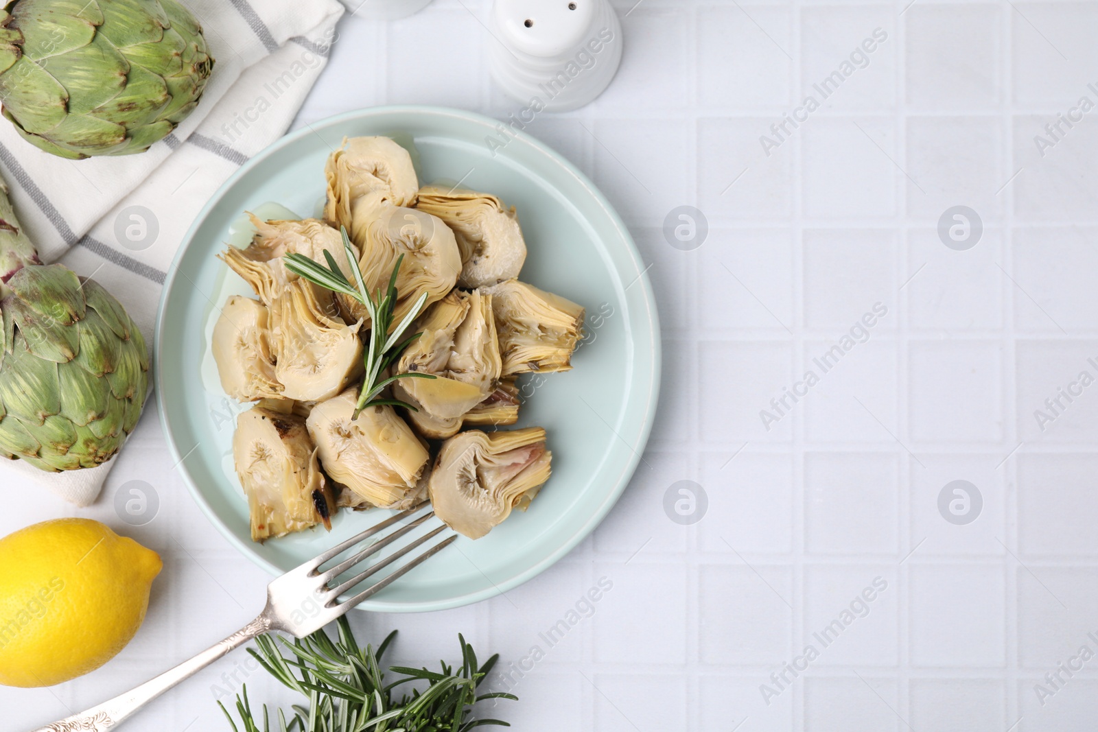 Photo of Pickled and fresh artichokes on white tiled table, flat lay. Space for text