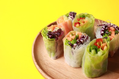 Different delicious spring rolls wrapped in rice paper on yellow background, closeup. Space for text
