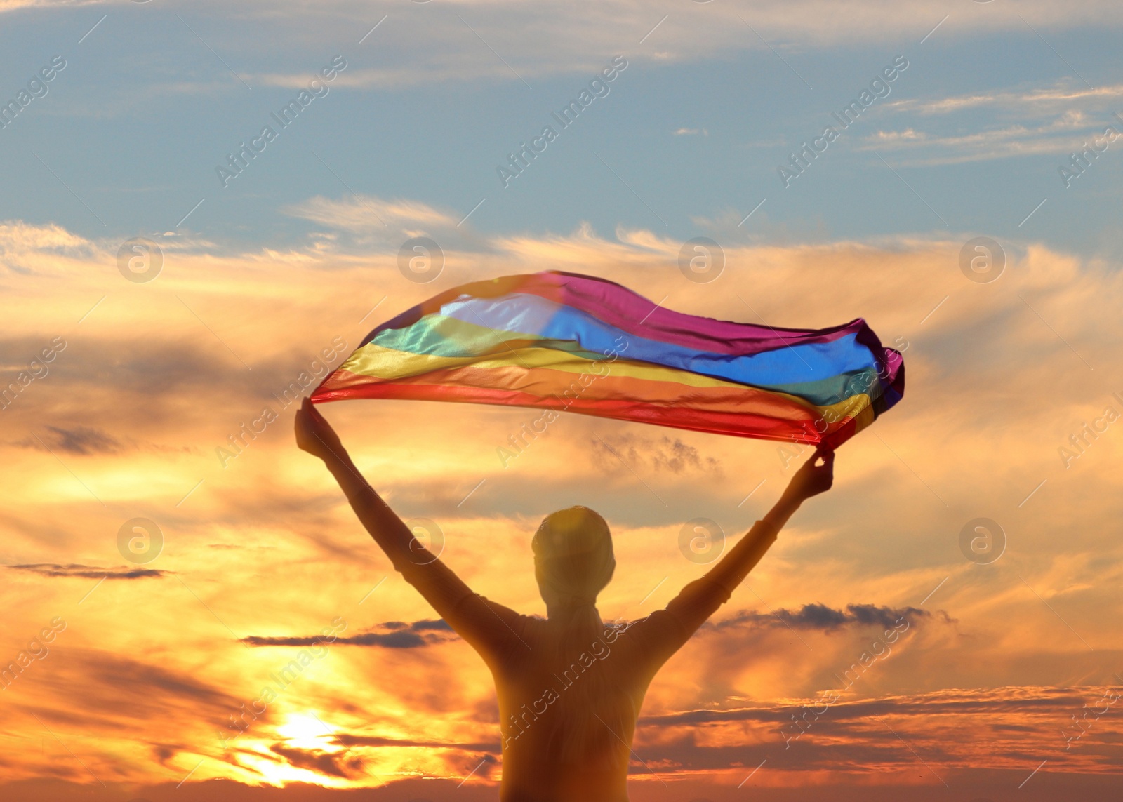 Image of Woman with bright LGBT flag against sky at sunset