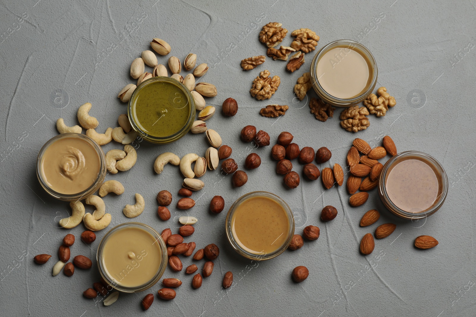Photo of Jars with butters made of different nuts and ingredients on grey table, flat lay