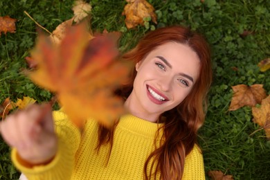 Photo of Smiling woman lying on grass and showing autumn leaf, top view