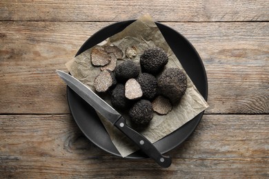 Photo of Black truffles and knife in plate on wooden table, top view