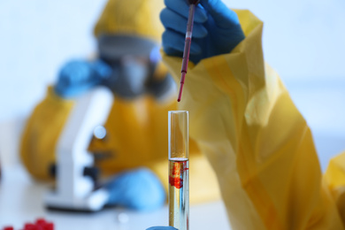 Photo of Scientist in chemical protective suit dripping blood  into test tube at laboratory, closeup. Virus research