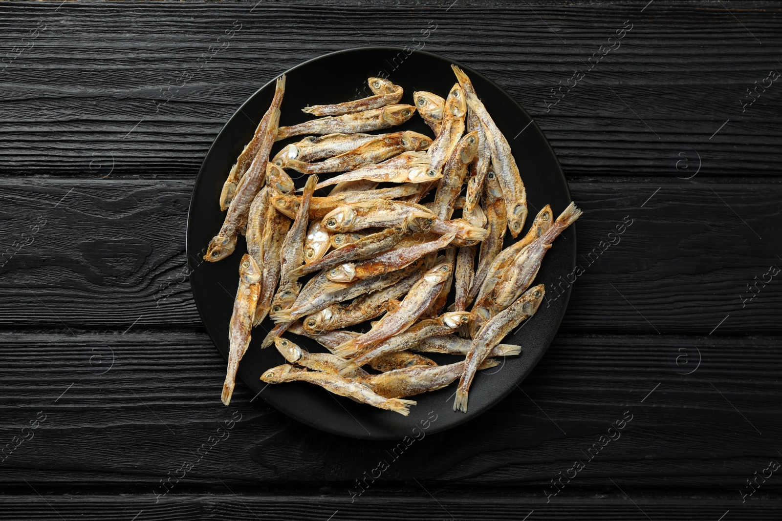 Photo of Delicious dried anchovies on black wooden table, top view