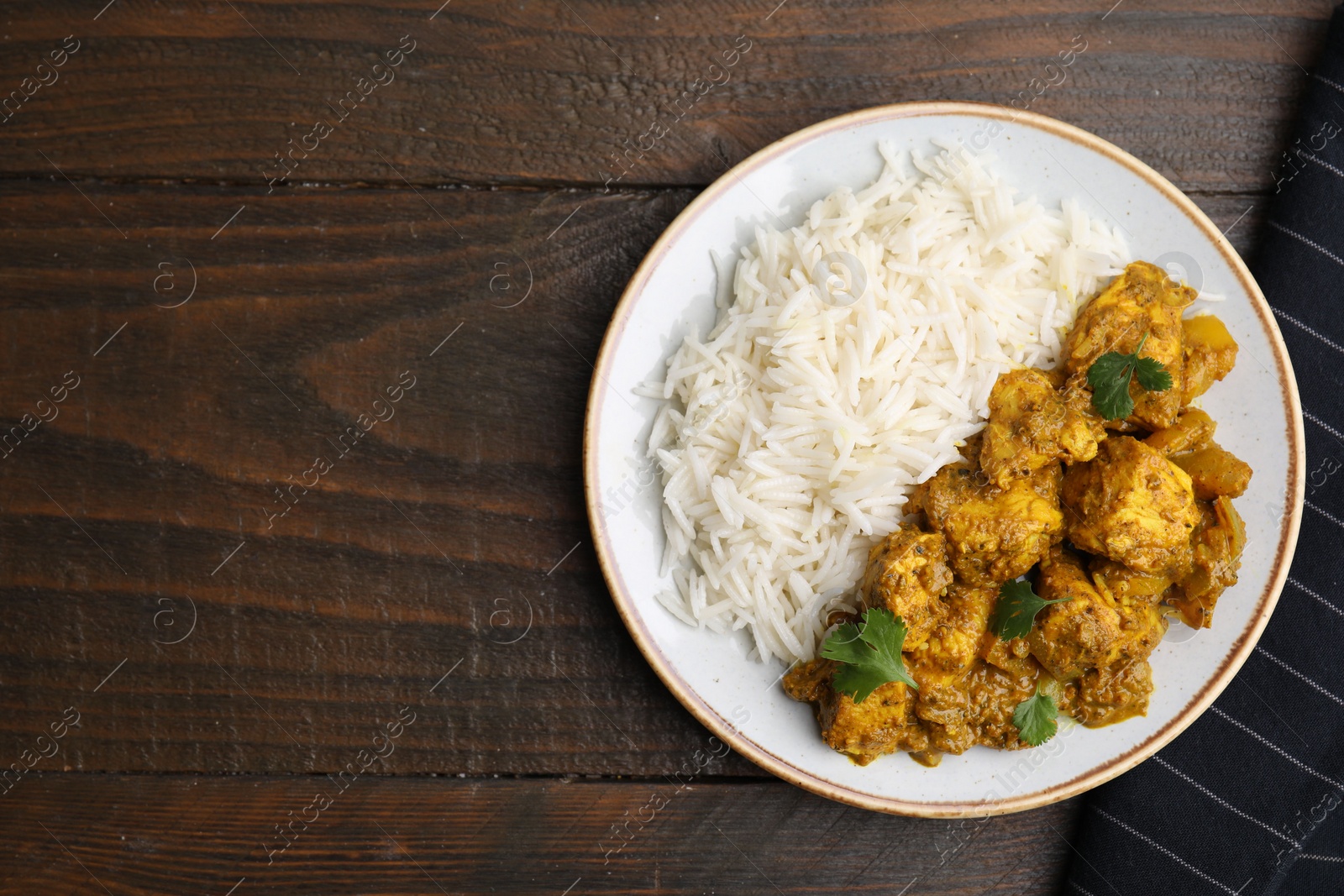 Photo of Delicious chicken curry with rice on wooden table, top view. Space for text