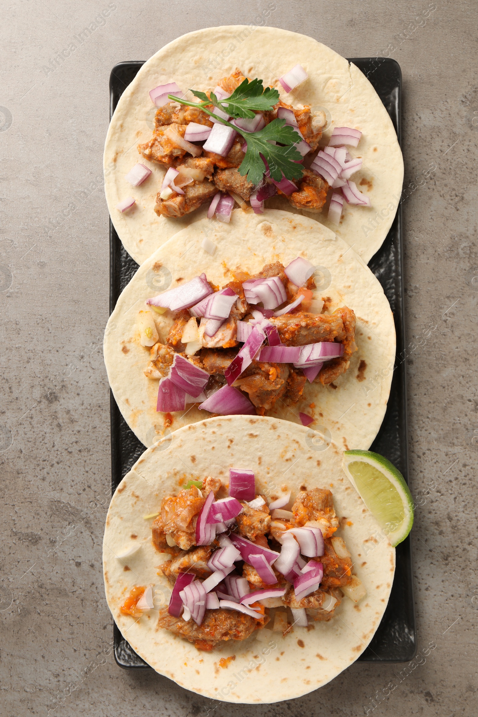 Photo of Delicious tacos with vegetables, meat and lime on grey textured table, top view