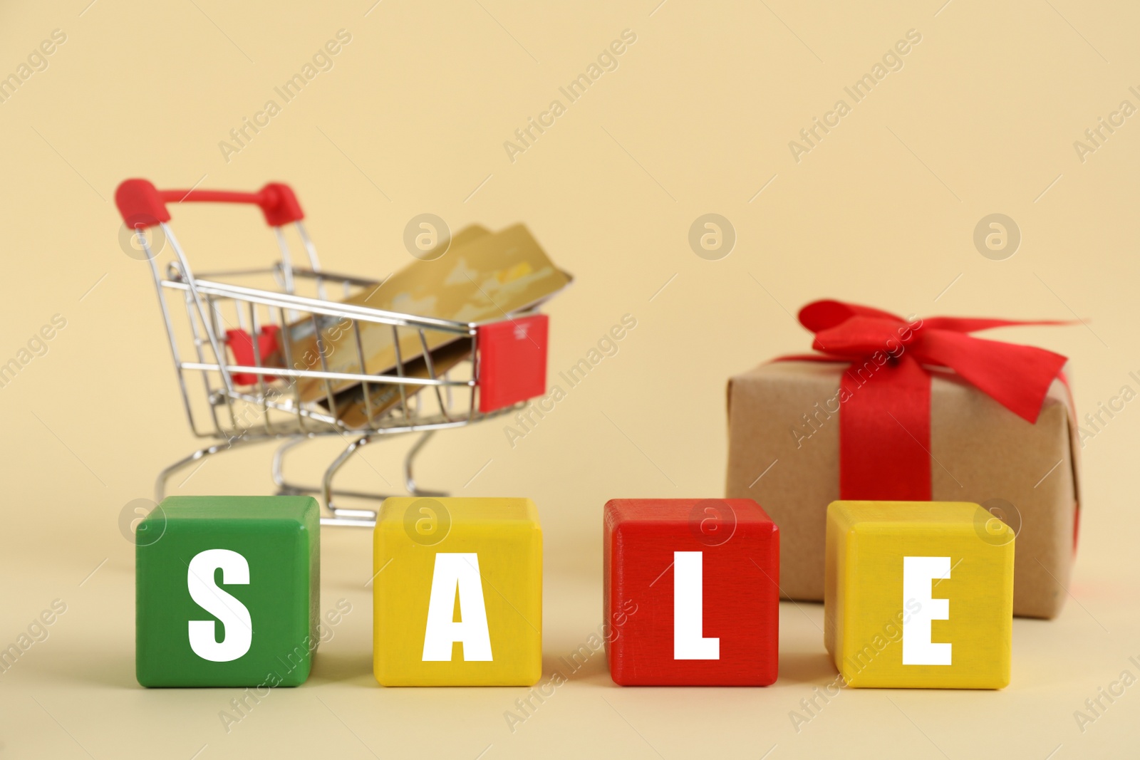 Photo of Word Sale made with colorful cubes, gift box and credit cards in shopping cart on beige background