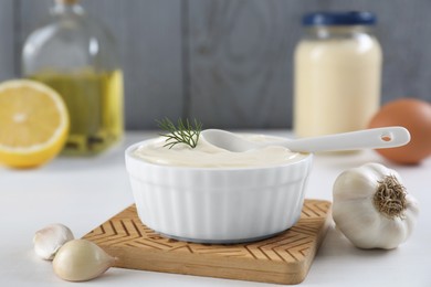 Photo of Fresh mayonnaise sauce in bowl and ingredients on white table