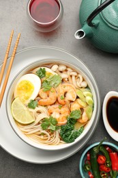 Photo of Delicious ramen with shrimps and egg in bowl served on grey table, flat lay. Noodle soup