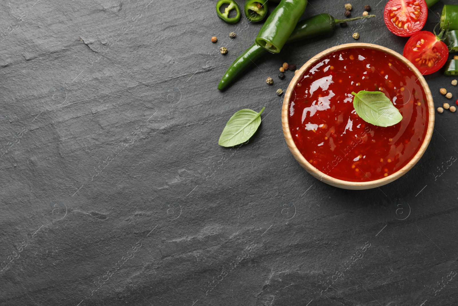 Photo of Spicy chili sauce and ingredients on black table, flat lay. Space for text