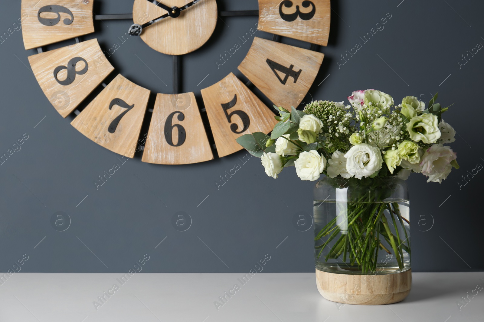 Photo of Bouquet with beautiful Eustoma flowers in vase on white table near grey wall