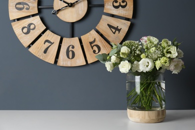 Bouquet with beautiful Eustoma flowers in vase on white table near grey wall