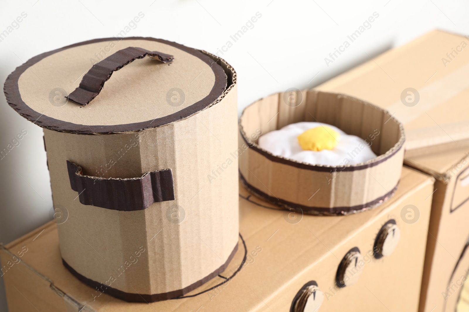 Photo of Cardboard stove with pot and frying pan near white wall