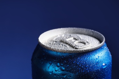 Aluminum can of beverage covered with water drops on blue background, closeup. Space for text