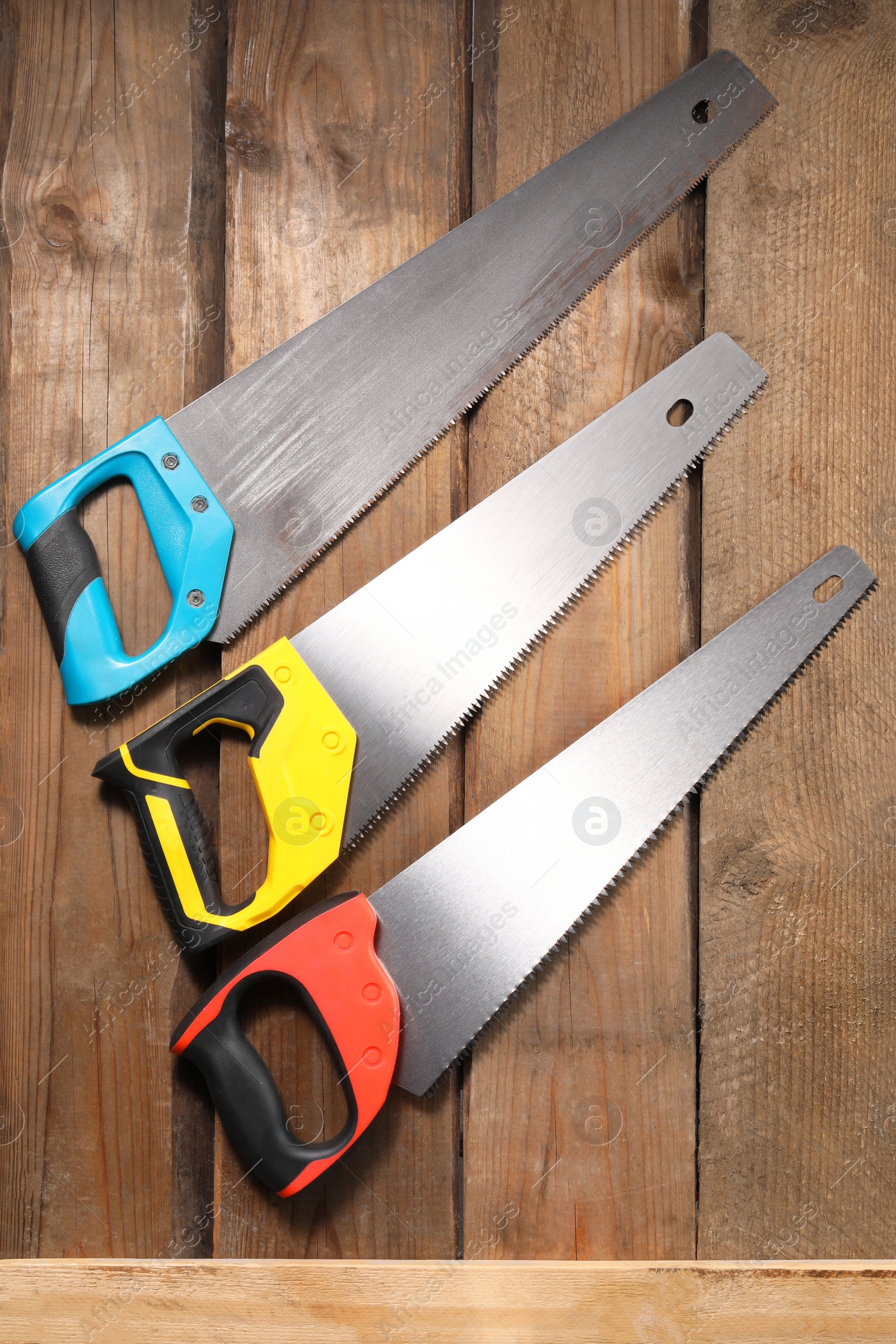 Photo of Saws with colorful handles on wooden surface, flat lay