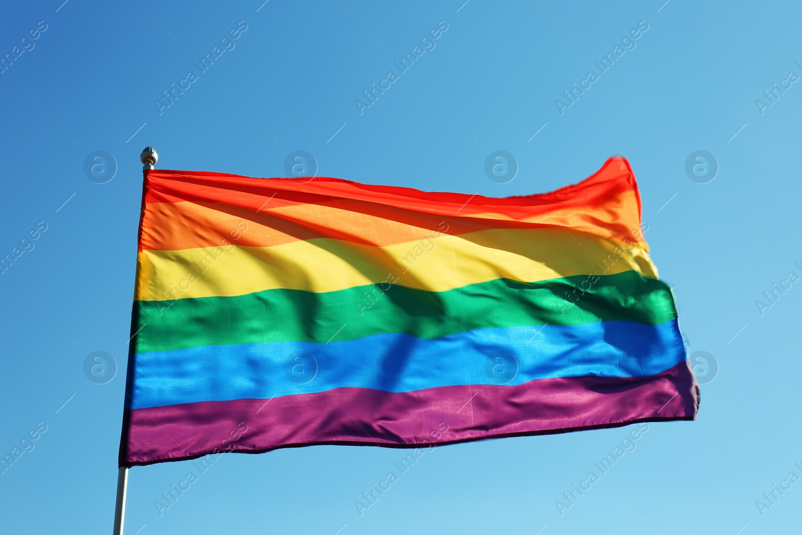 Photo of Rainbow LGBT flag fluttering on blue sky background. Gay rights movement