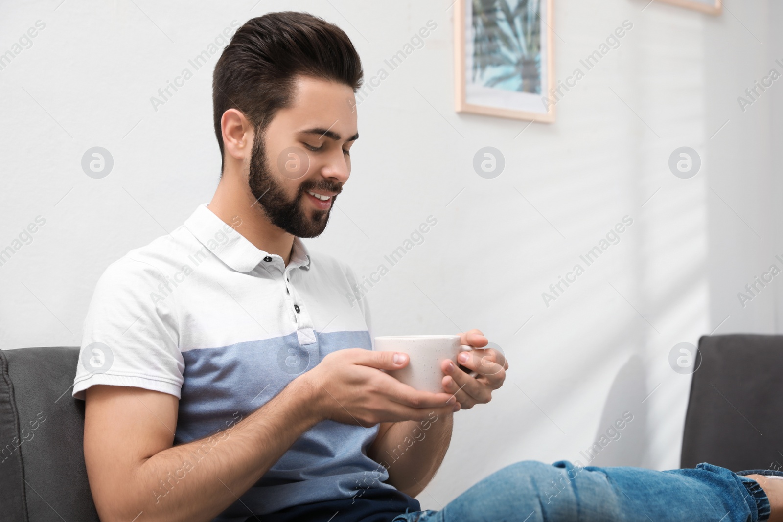 Photo of Young man with cup of drink relaxing at home