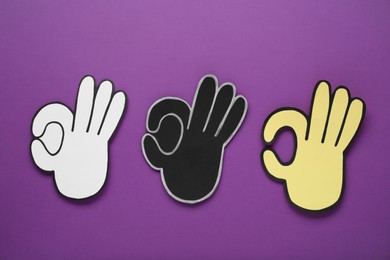 Photo of Paper cutouts of Okay hand gesture on purple background, top view