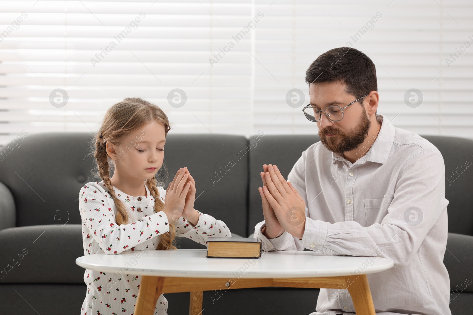 Photo of Girl and her godparent praying over Bible together at table indoors