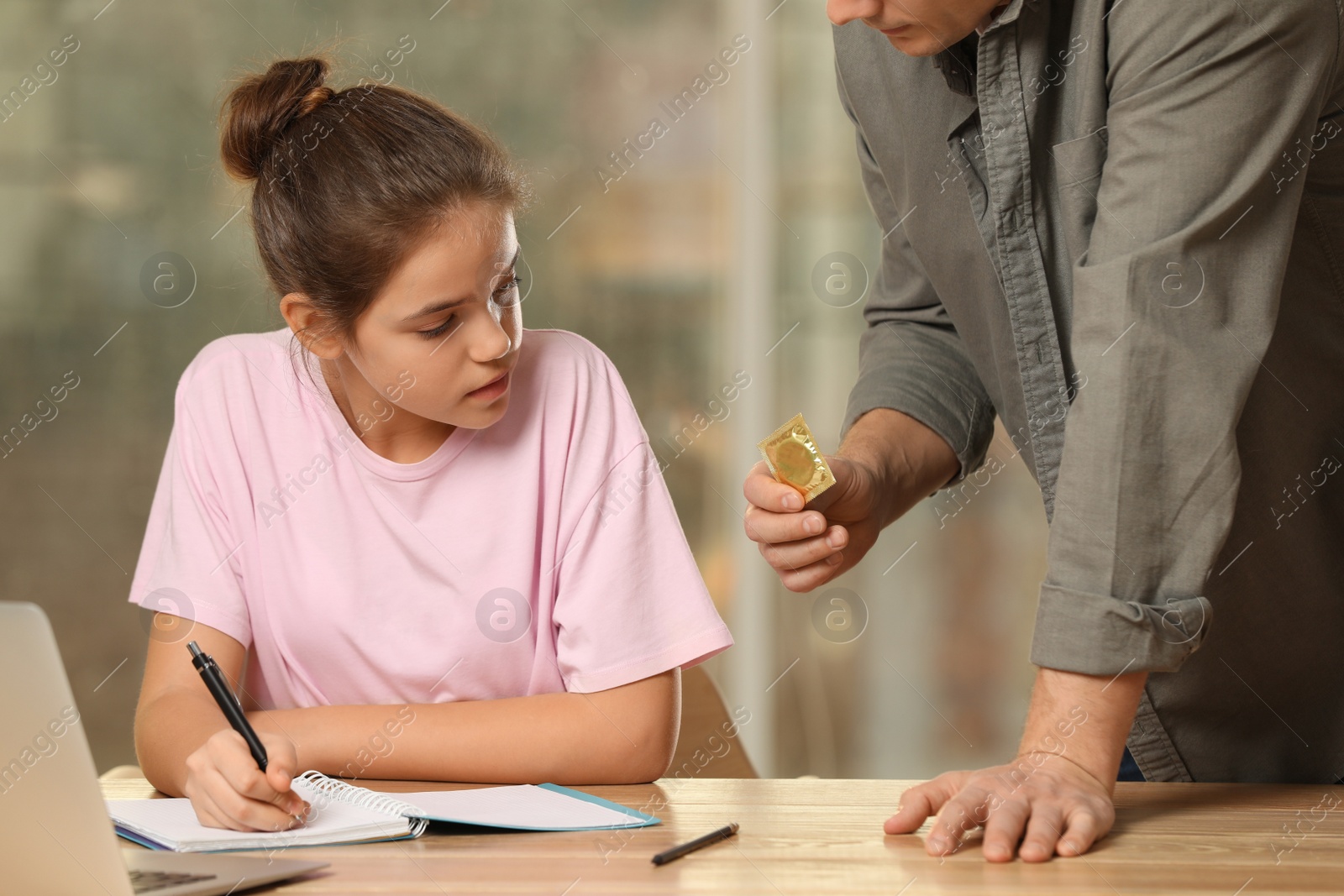 Photo of Father talking with his teenage daughter about contraception while she doing homework at home. Sex education concept