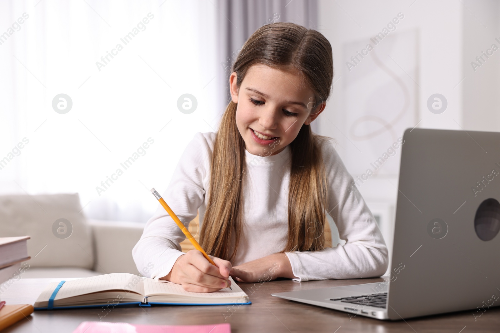 Photo of E-learning. Cute girl taking notes during online lesson at table indoors