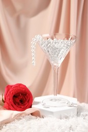 Photo of Martini glass with pearl beads and red rose on pink cloth