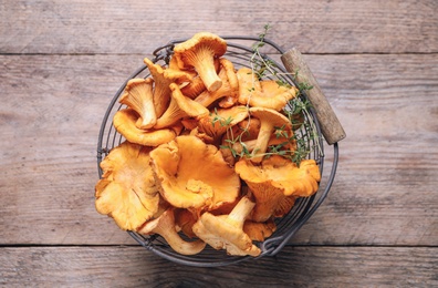 Photo of Fresh wild chanterelle mushrooms in metal basket on wooden table, top view
