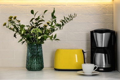 Modern yellow toaster, coffeemaker and beautiful bouquet on countertop in kitchen