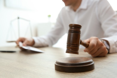 Photo of Judge with gavel at table in courtroom, closeup. Law and justice concept