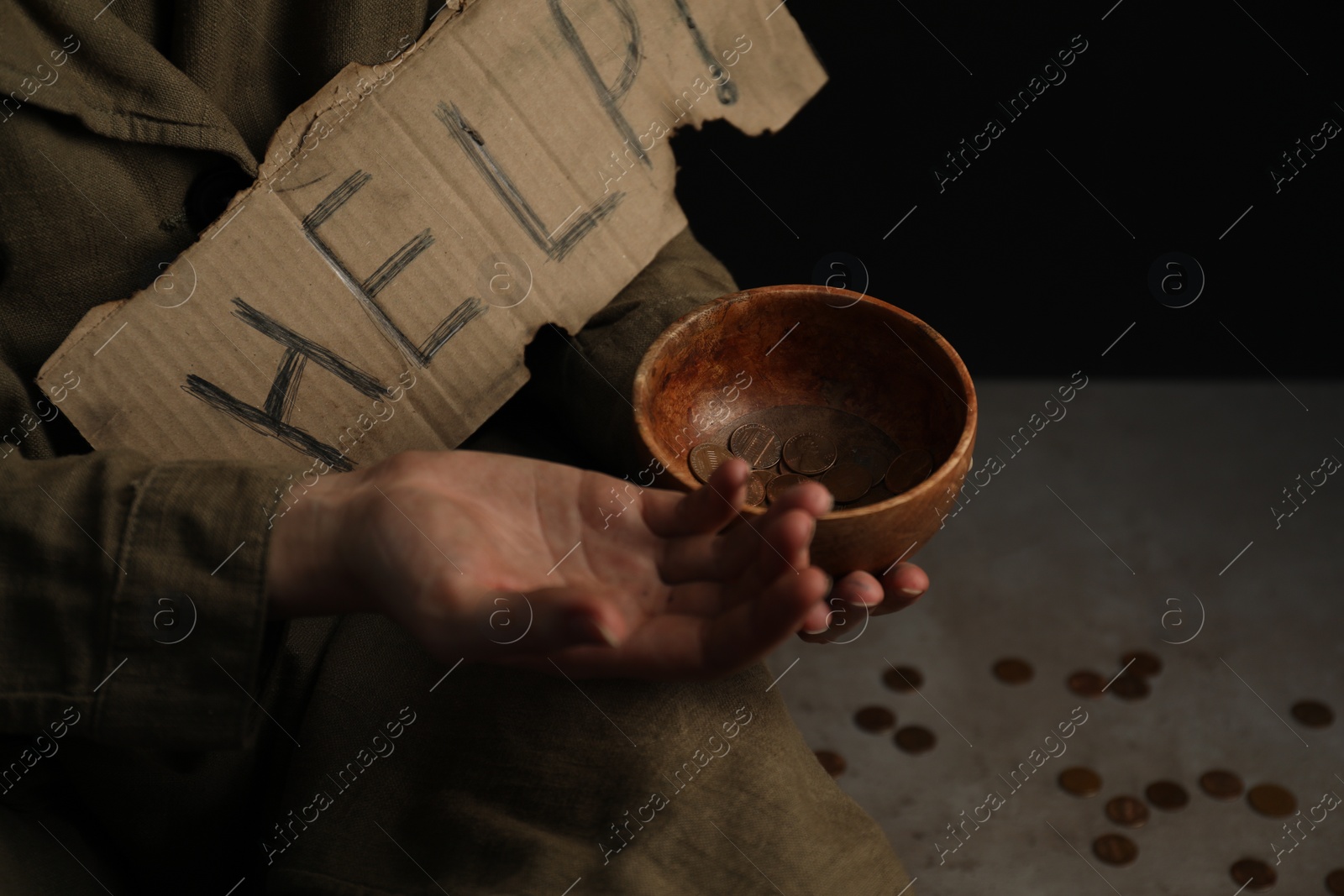 Photo of Poor homeless woman with help sign holding bowl of donations on floor, closeup