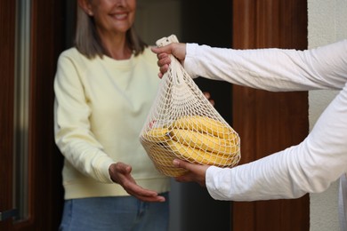Helping neighbours. Man with net bag of products visiting senior woman outdoors, closeup