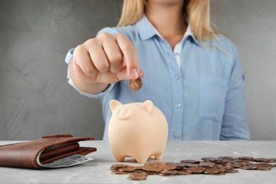 Photo of Woman putting coin into piggy bank on grey stone table, closeup view