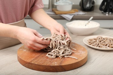 Photo of Woman making soba (buckwheat noodles) at wooden table in kitchen, closeup